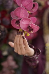 Woman's Hand with Dark Manicure and Glitter Near Bright Pink Orchid Flowers