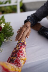 Close up of Two Hands, One in Batik, Gently Held Together on a White Tablecloth