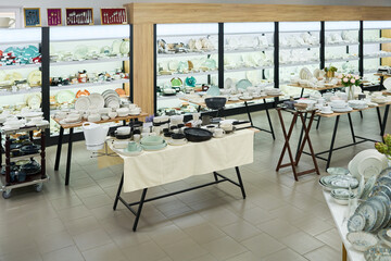 Ceramic tableware displayed on tables and shelves in store showroom, various plates, bowls, cups, and serving dishes arranged for sale, bright retail environment, no people visible
