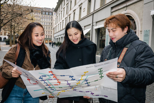Asian travelers exploring a city while reading a metro map together. Concept of navigation, tourism, friendship, teamwork, and urban adventure during an international trip.
