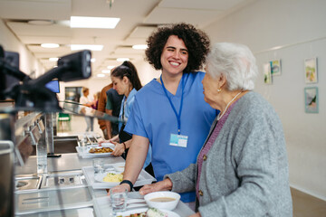 Obraz premium Senior woman having lunch with supportive caregiver in community center cafeteria.
