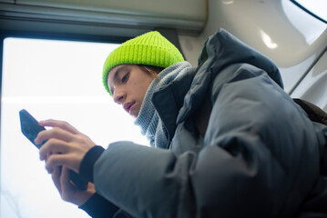 A teenage boy in winter clothes holds a phone in his hands, surfs the Internet, a child sits on a bus, goes to school.