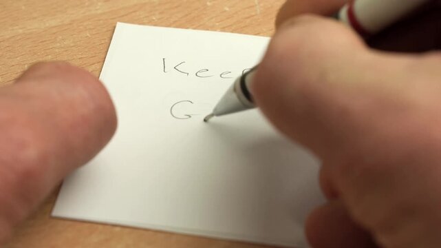 Caucasian man writing a note with Keep Going text with a pencil.