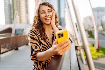 A cheerful woman poses on the street with a phone against the backdrop of a bustling metropolis. A...