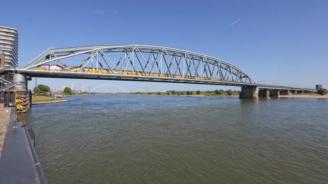 A yellow passenger train crossing the historic Spoorbrug (railway bridge) over the Waal river in Nijmegen, Netherlands