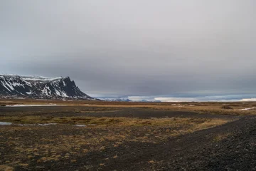Ingelijste posters Huisarts Die dunklen Klippen der Halbinsel Snæfellsnes erheben sich imposant aus der flachen Ebene. Der graue, eintönige Wolkenschleier hängt tief und ist fast zum Greifen nah.  © Stephanie