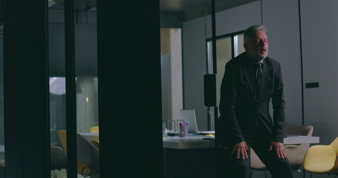 Frustrated businessman leaning forward with hands clenched in emotional moment inside modern office boardroom after corporate meeting