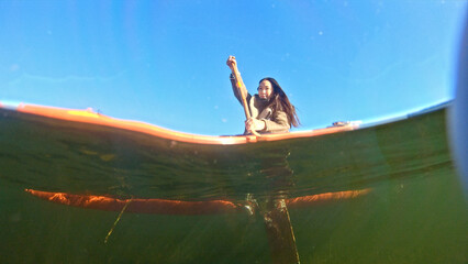 A woman paddles a canoe on a serene lake, embodying tranquility and adventure. The clear blue sky and calm water reflect her focused effort, capturing the essence of outdoor activities.