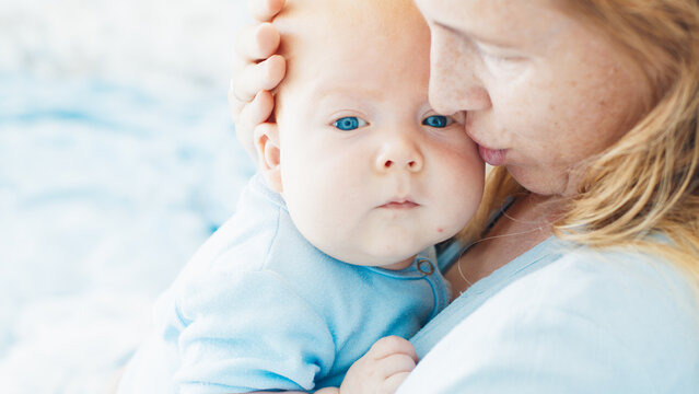 Mother caresses her newborn son with deep blue eyes in a bright room