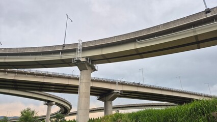 Modern elevated highway bridge with concrete supports framed against a bright sky, captured in a wide architectural view.