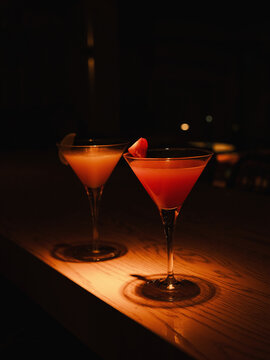 Two stylish cocktails in martini glasses sit on a softly illuminated bar surface, creating a warm, intimate nighttime atmosphere perfect for relaxing or celebrating.
