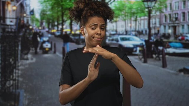 Woman with hands in t for timeout on city street, wearing black t shirt and looking skeptical while making a stop gesture; dismissal.