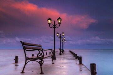 Seaside pier at sunset with metal benches and glowing lamps stretching into the calm water in Sveti Vlas, Burgas, Bulgaria