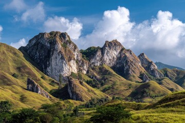 Fototapeta premium Rolling green hills with prominent rocky peaks under a bright blue sky with clouds