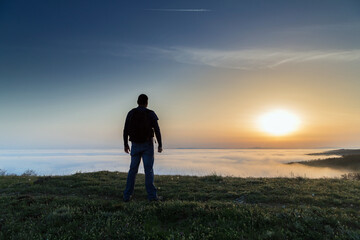 Back view of man on the hill over the fog at sunset. Sofia, Bulgaria