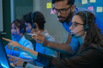 Customer support team in a modern call center receiving guidance from a supervisor. Diverse employees working with headsets and computers, representing teamwork, communication, and business