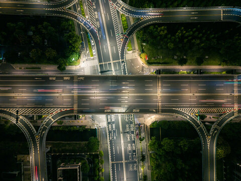 Aerial view of a busy highway intersection at night in an urban area, with moving car light trails.