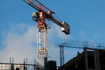 Control Cabin and Counterweight of Red Tower Crane at Construction Site. Monolithic Box with Window Holes and Rebar outlets against Blue Sky background.