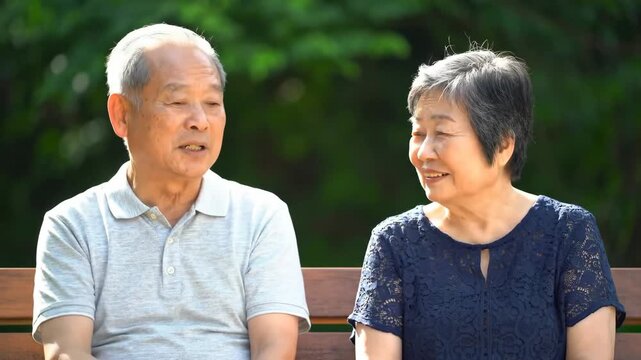 Asian senior couple sitting & talking on a park bench, greenery in the background, for retirement or lifestyle images
