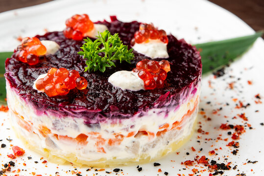 "Herring Under a Fur Coat" (Shuba) salad, featuring distinct layers of beets, carrots, potatoes, and herring, elegantly garnished with red caviar and parsley on a white plate.