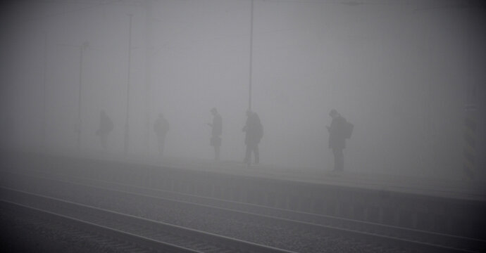 Silhouettes of commuters waiting on a foggy railway platform with poor visibility in the early morning light