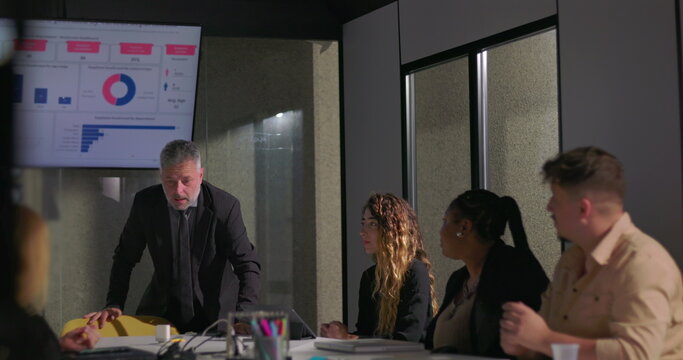 Frustrated manager holding head in hands during tense office meeting as disheartened team reacts to stressful performance review