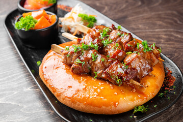 Juicy grilled meat skewers, likely beef or lamb kebab, served on warm, soft flatbread and garnished with fresh parsley and sesame seeds on a dark plate