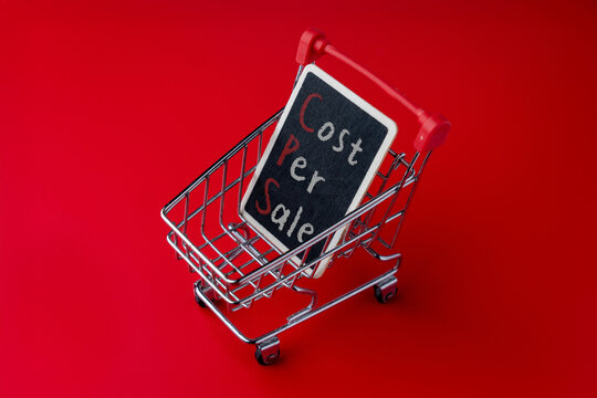 A shopping cart and a blackboard displays the text Cost Per Sale. Digital advertising metrics, e-commerce performance, and retail analytics concept.