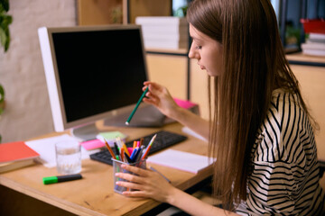Young woman selecting stationery at desk during home study session. Concept of education workflow, productivity planning, creative routines, and modern remote learning atmosphere.