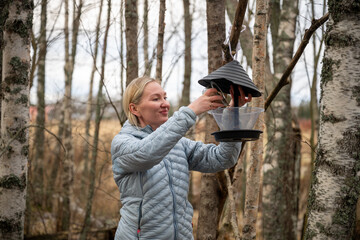 Woman refilling bird feeder in autumn forest