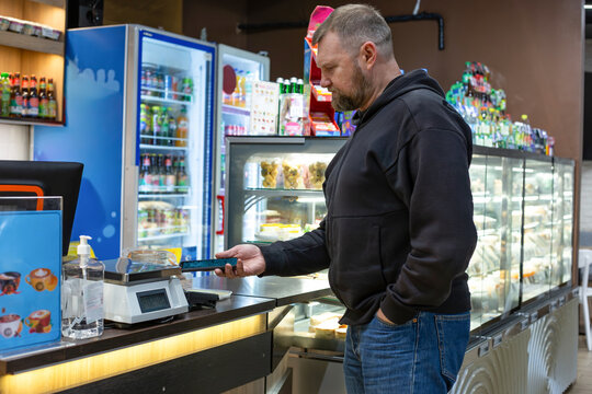 Man paying for desserts in a cafe using his smartphone with NFC. He holds the phone over the payment terminal at the counter. Modern cashless transaction, customer service, retail environment. - Powered by Adobe
