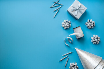Shiny party silver streamers with confetti and cones on blue background, top view