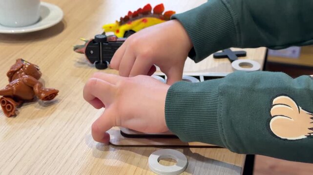 IMG_8712Child playing a wooden tic tac toe game at a table with toys around. Closeup hands placing pieces on the board during fun educational indoor playtime.