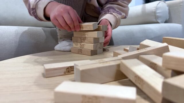 Child building a wooden block tower at a table. Closeup hands stacking and arranging wooden pieces during fun educational indoor playtime.