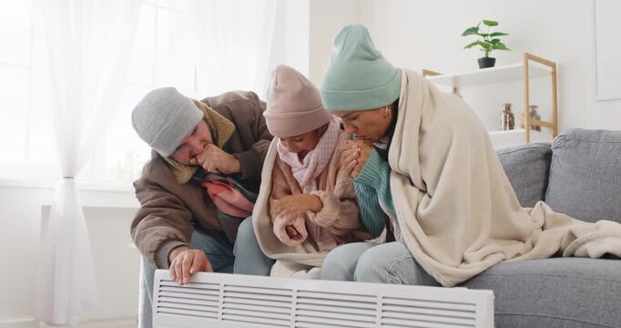 Family huddles by heater in cold. Wrapped in a blanket, they warm hands in the living room as winter drafts linger. Home heating saves energy, adds warmth. Concept: survival in a cold home.