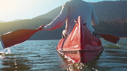 A person paddles a red canoe on a serene lake, surrounded by forested mountains. The scene captures a peaceful outdoor activity, ideal for those seeking a tranquil weekend escape.