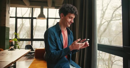 Smiling young man typing on smartphone using mobile app in modern apartment - Powered by Adobe