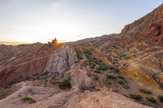 Erosion landscape of red and yellow sandstone, rock formations at sunrise with sun star, Skazka Canyon, fairytale gorge, Tosor, Kyrgyzstan