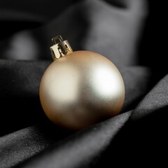 Elegant single gold Christmas bauble ornament resting on a luxurious draped black silk fabric background