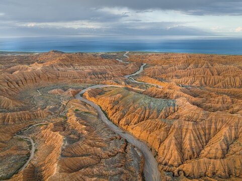River bed runs through a landscape of eroded hills, badlands, Issyk Kul Lake in the background, aerial view, Canyon of the Forgotten Rivers, Issyk Kul, Kyrgyzstan