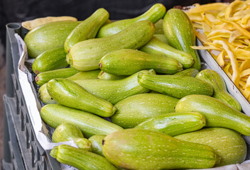 Fresh green zucchini with vegetables at a local farmers' market outdoors in daylight. Organic harvest, healthy food, and seasonal produce. Zucchini at the grocery store.