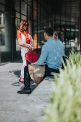 Obraz premium A stylish red-haired woman stands with a red handbag, chatting with two seated colleagues outside a glass-walled office.