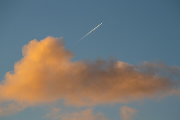 Airliner contrail above warm evening cloud