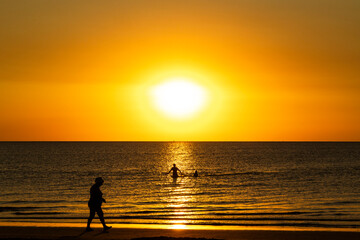 Fototapeta premium Golden light bathes the shoreline as beachgoers enjoy a tranquil morning swim and walk by the sea during sunrise in Cyprus.