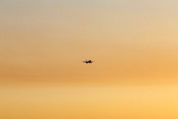 Passenger aircraft approaching or departing under a gradient orange sky, captured in a minimal and peaceful moment.