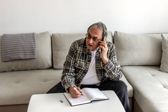 Smartphone, budget planning and senior man in living room for retirement research, website investment information or asset management. Elderly person writing notes, using phone online finance banking.