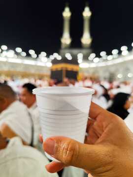 Plastic Glass of Zamzam Water held in front of the Kaaba during night prayer in the Grand Mosque area with a blurred background