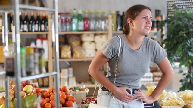 Young woman feels cramps and a painful period in the supermarket. Woman holds her lower abdomen with hands during painful menstruation. High quality 4k footage