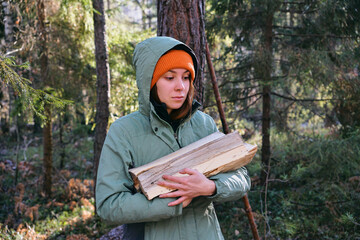A young woman carries firewood in her hands in the forest. The concept of preparing firewood for...