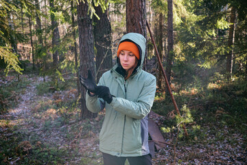 A young woman puts on fleece gloves in the forest. Camping insulation, outdoor clothing © Akhtiamova
